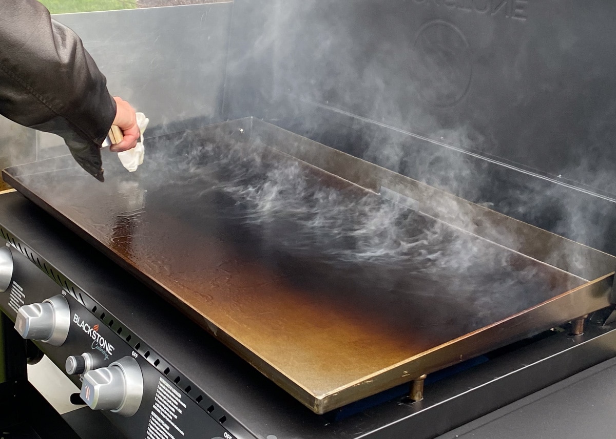 closeup of a blackstone griddle being seasoned with smoke rising off of the cooking surface