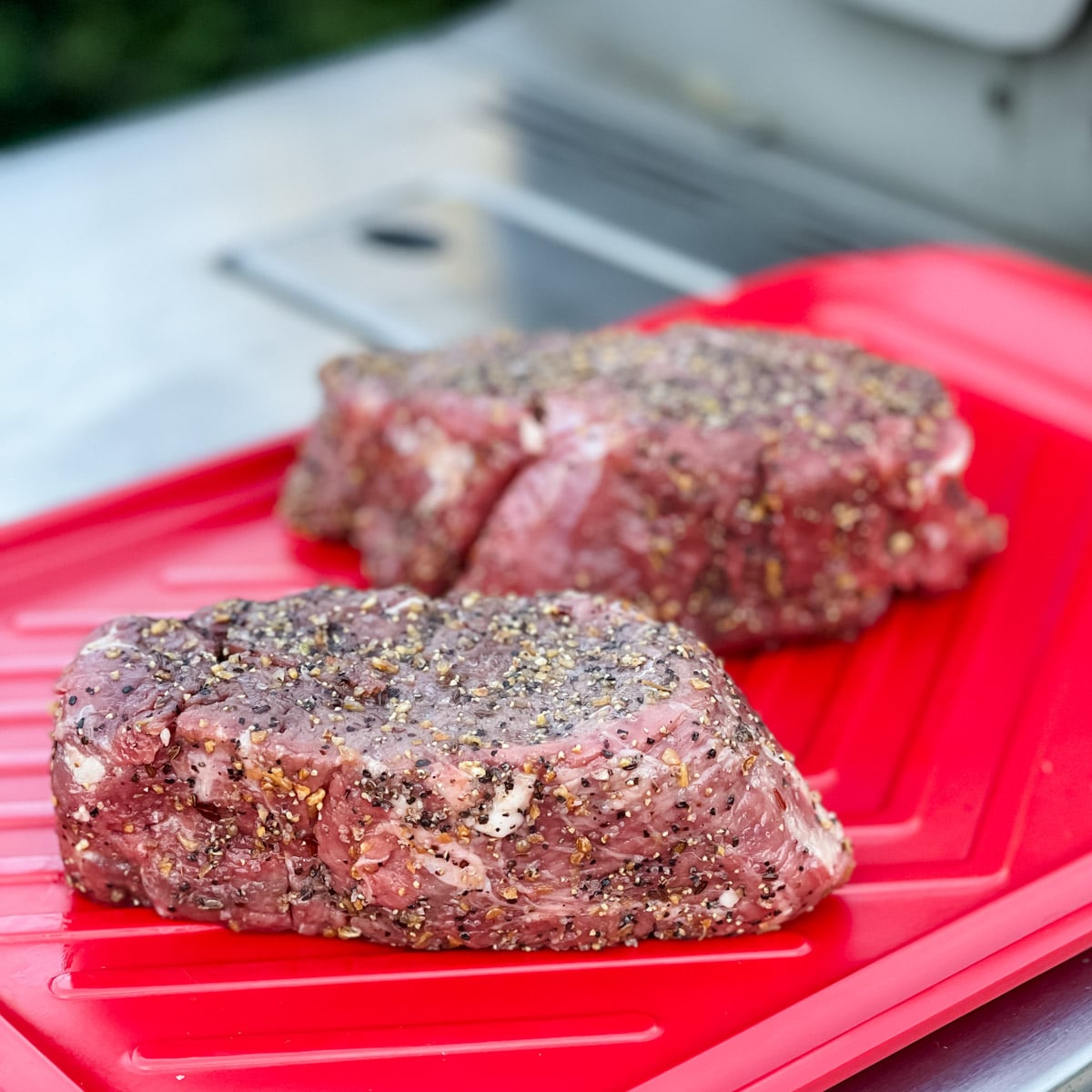 raw steaks seasoned with Montreal rub on a red prep board