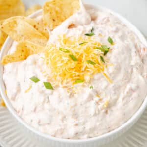 boat dip in a white bowl topped with shredded cheese and scallions with tortilla chips
