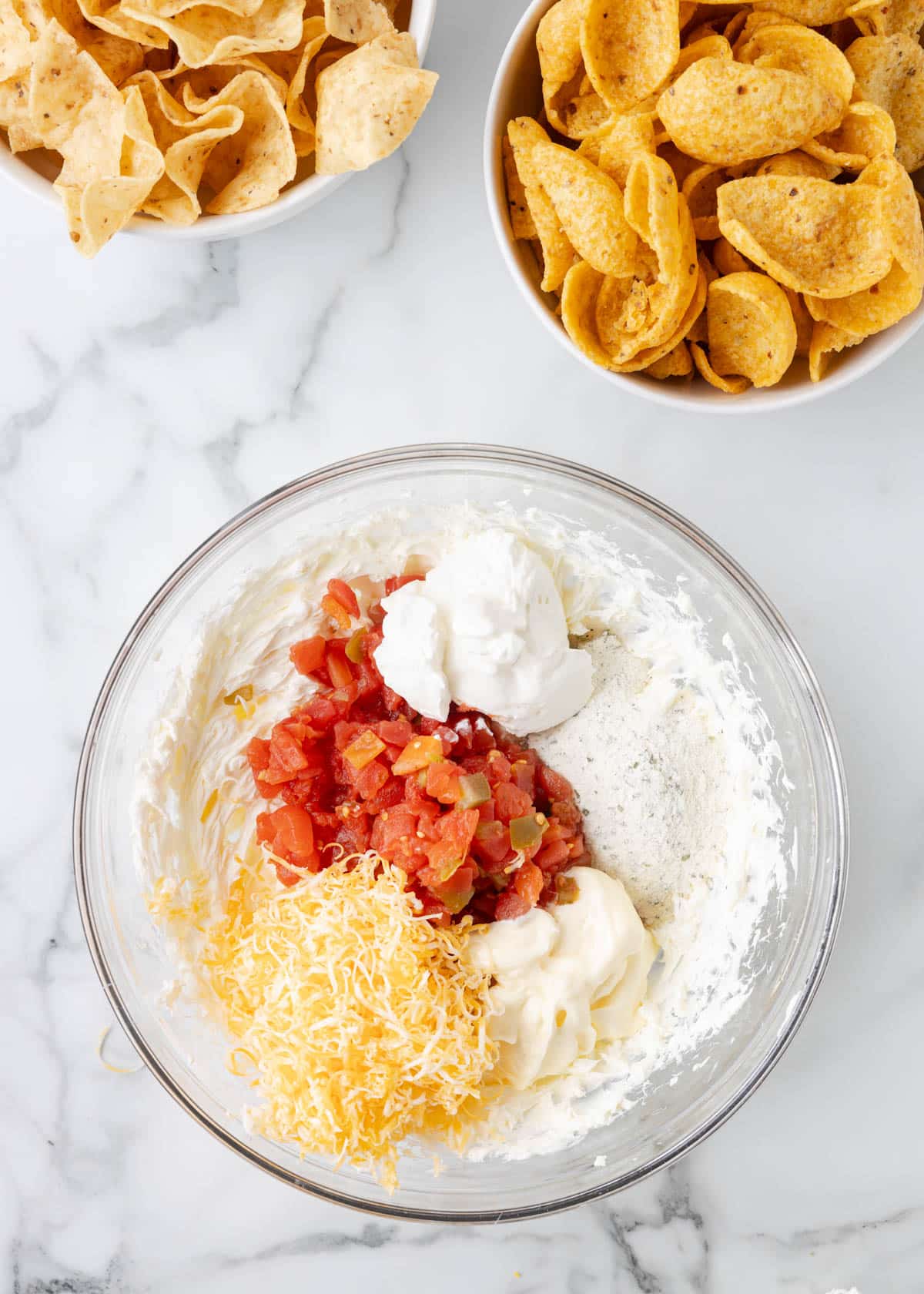 overhead of unmixed Boat Dip ingredients in a glass bowl on a marble board next to two bowls of corn chips