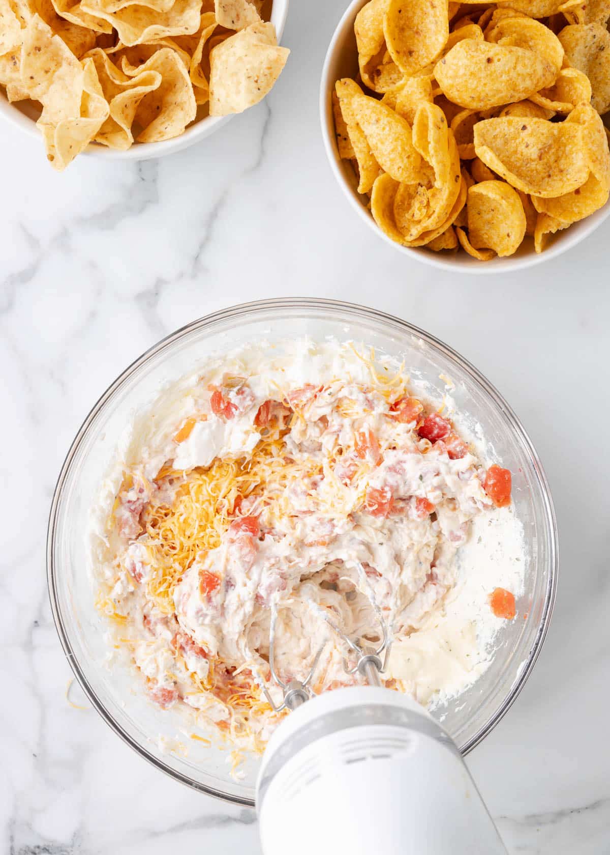 overhead of Boat Dip being combined with a hand mixer in a glass bowl