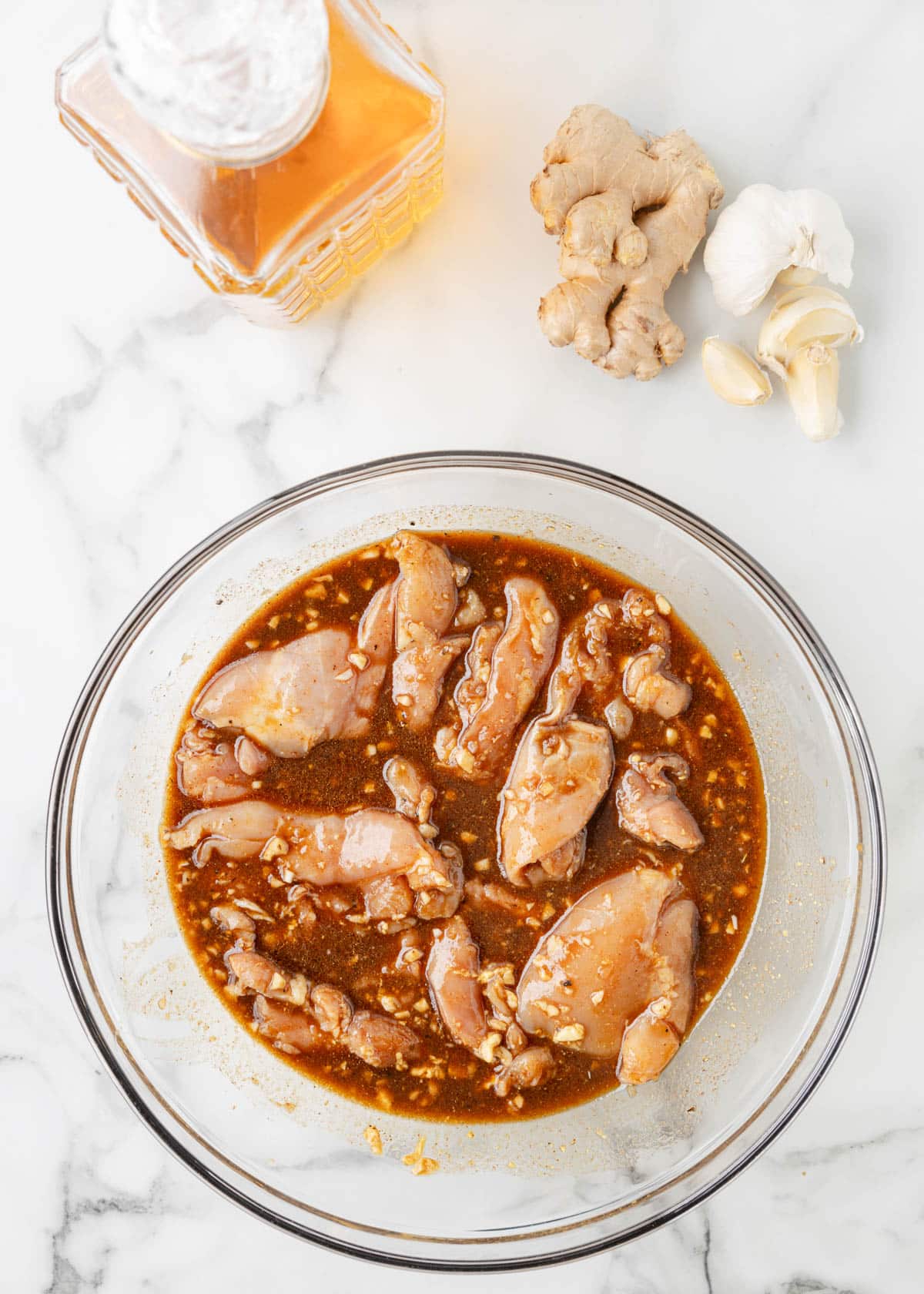 overhead of raw chicken thighs coated with bourbon marinade in a glass bowl