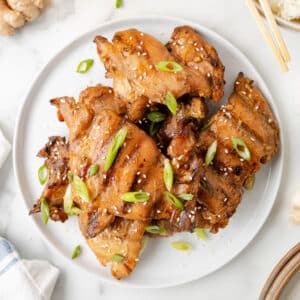 grilled bourbon chicken thighs on a white plate garnished with scallions and sesame seeds