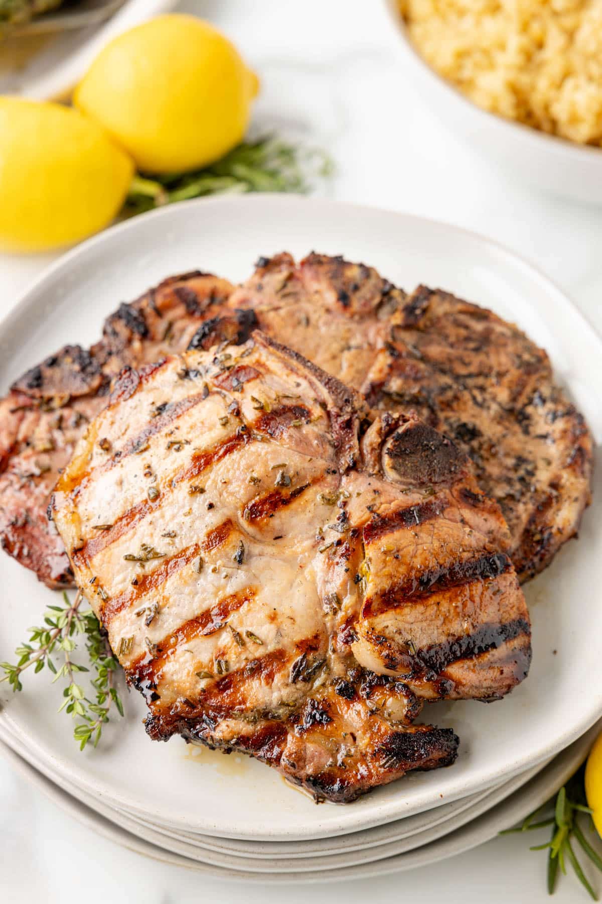 two grilled lemon pork chops on a white plate with sprigs of fresh thyme