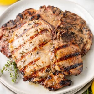 grilled lemon herb marinated pork chops on a white plate with sprigs of fresh thyme