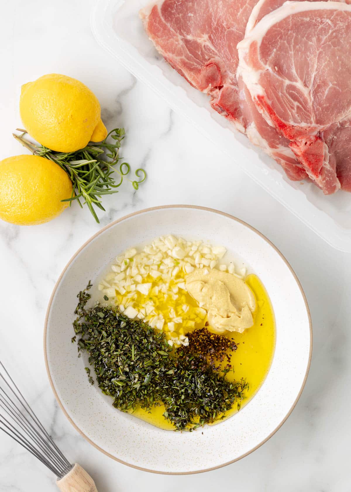 overhead of olive oil, chopped garlic, dijon, and chopped herbs in a white bowl