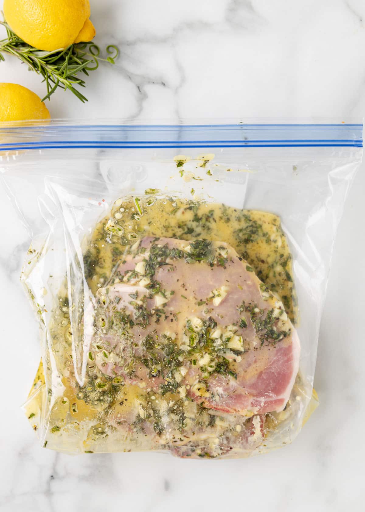 raw pork chops with lemon garlic herb marinade in a sealed plastic zip top bag