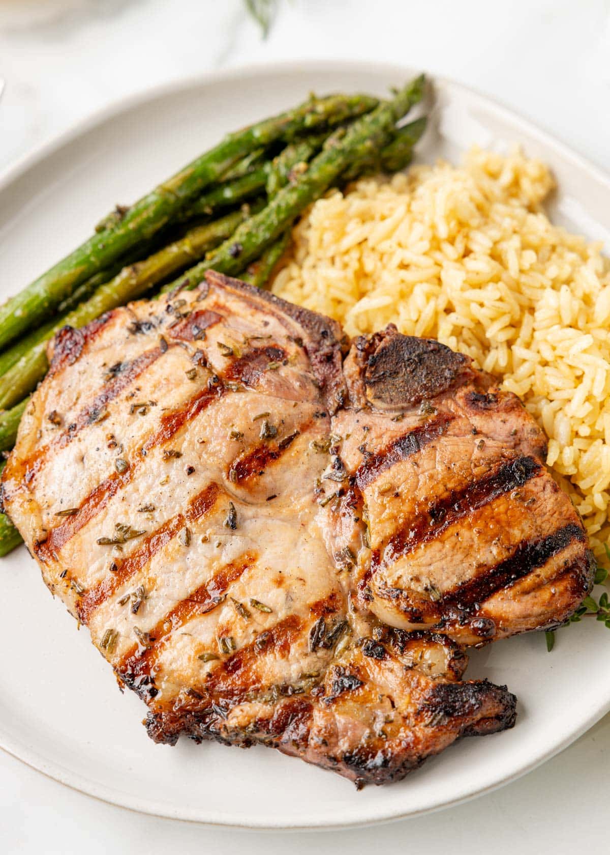 lemon herb pork chop on a white plate with asparagus and rice pilaf