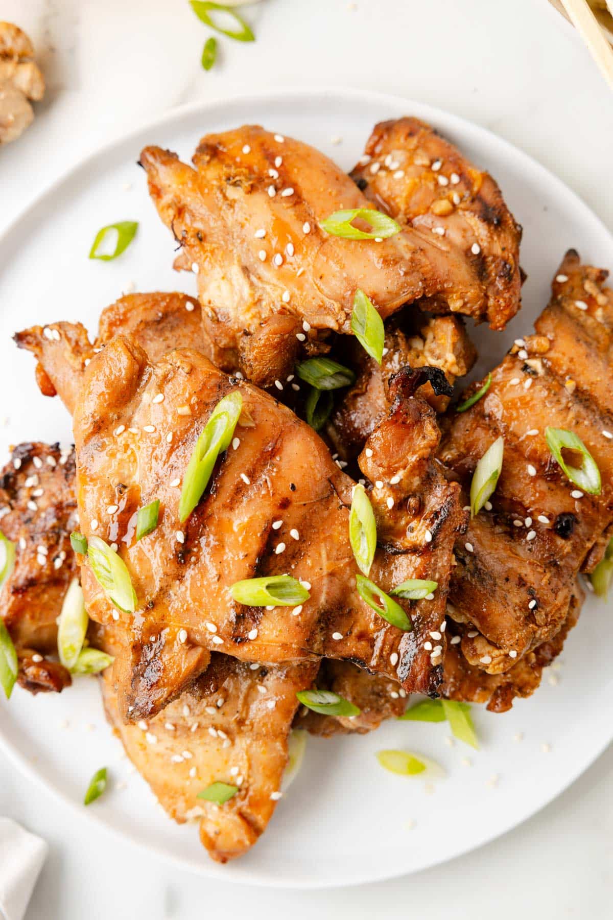 grilled bourbon chicken thighs on a white plate garnished with scallions and sesame seeds