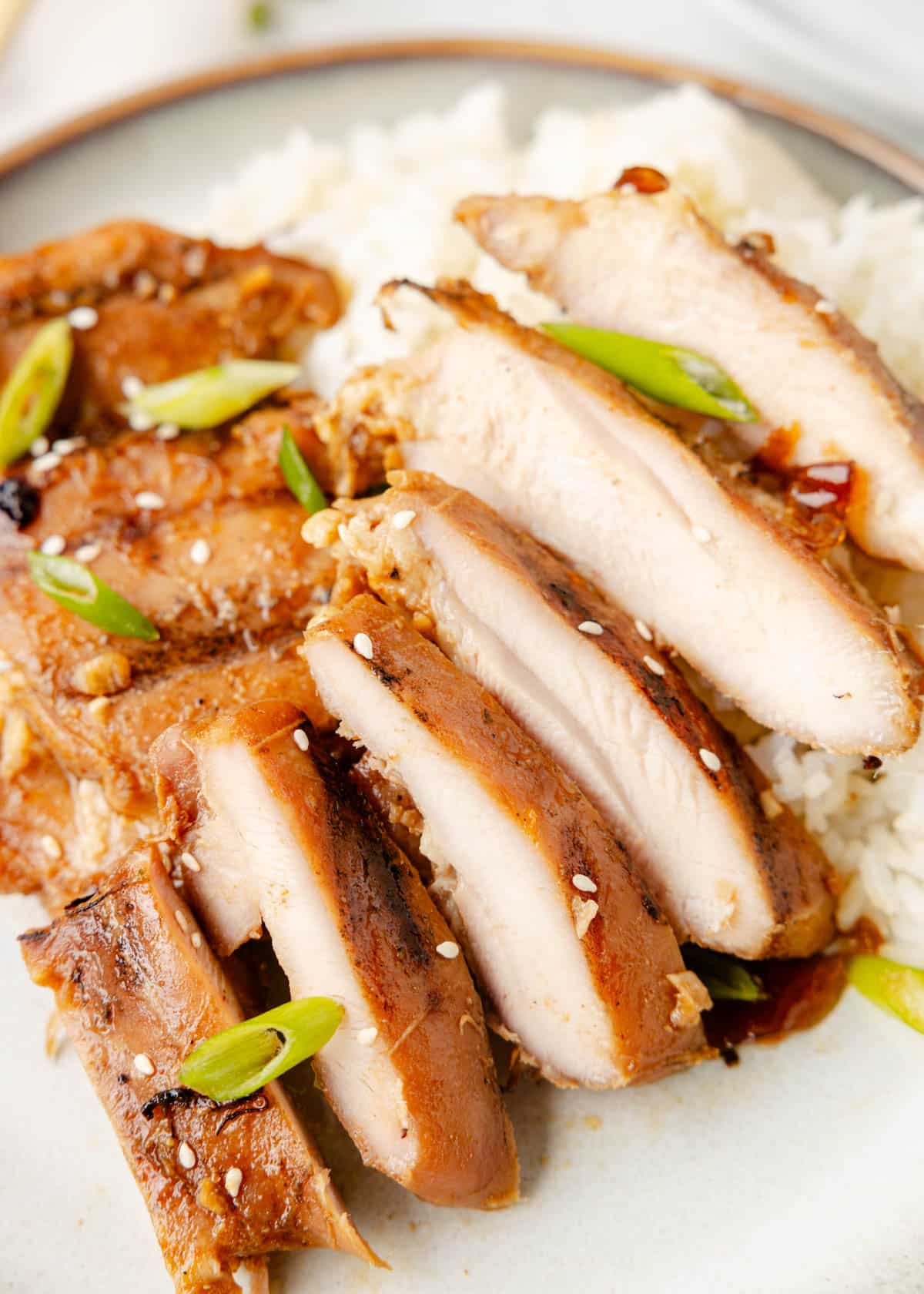 grilled bourbon chicken thigh sliced on a plate with white rice