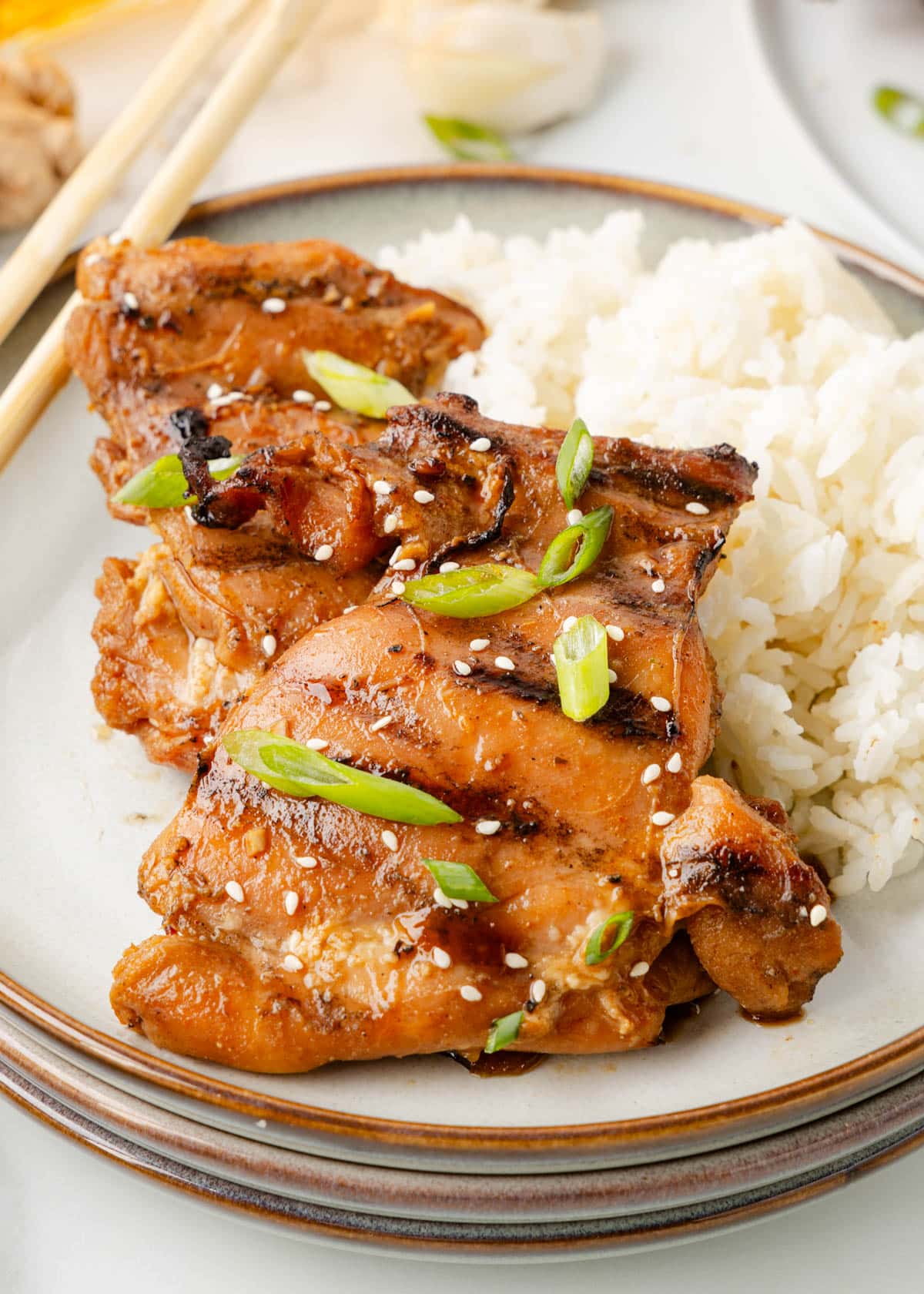 grilled bourbon chicken thighs on a white ceramic plate with white rice and chopsticks