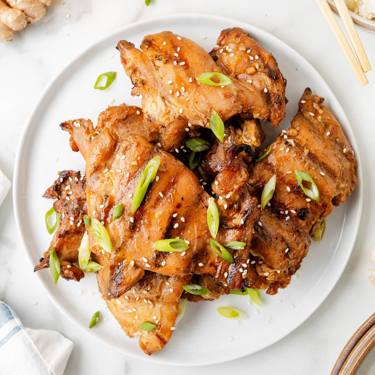 grilled bourbon chicken thighs on a white plate garnished with scallions and sesame seeds