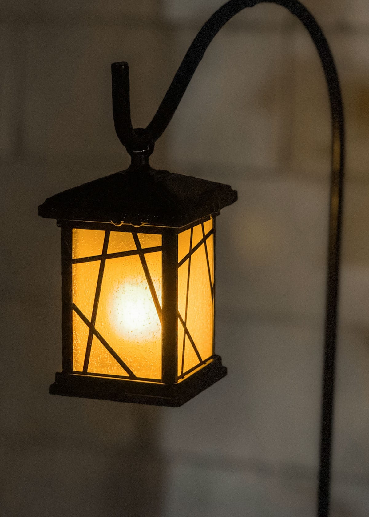 lit solar powered lantern hanging from a shepherd's hook at night