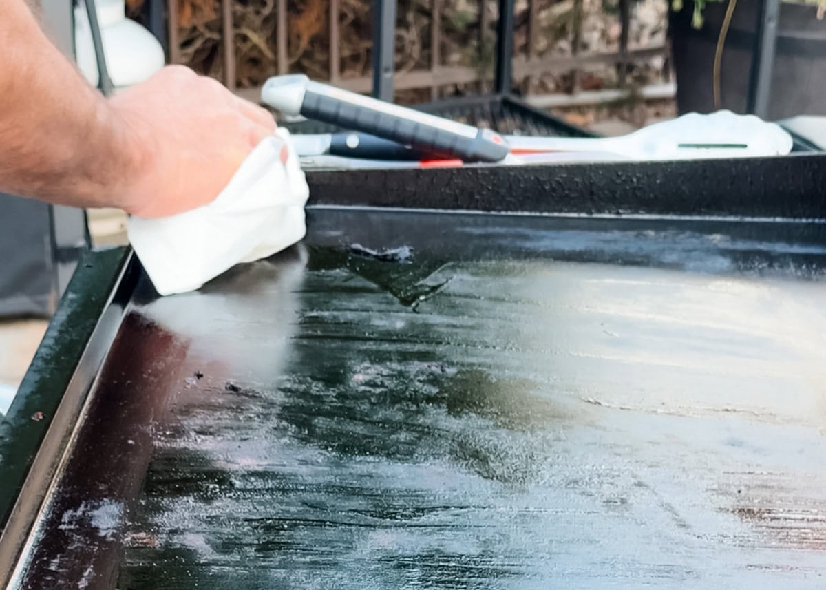 removing excess oil from a griddle with a paper towel after scraping