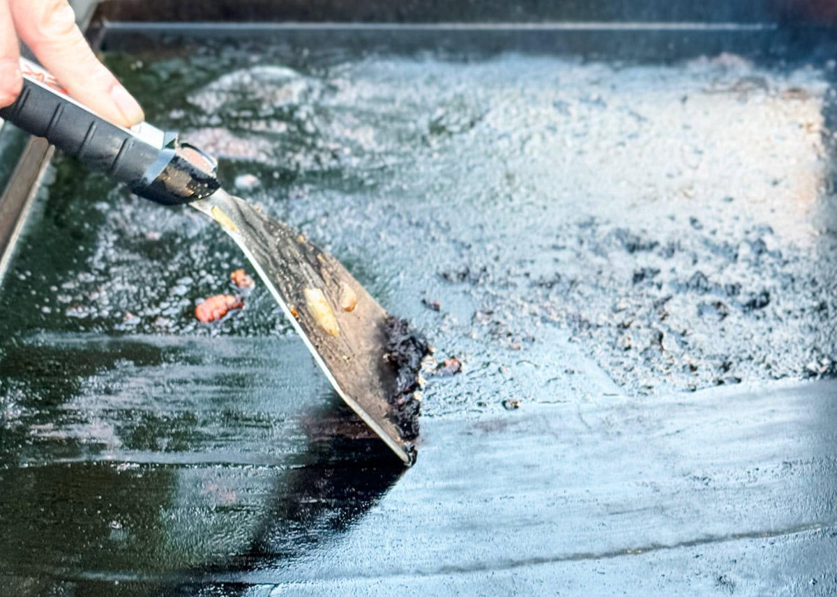 dirty griddle surface being scraped with a spatula