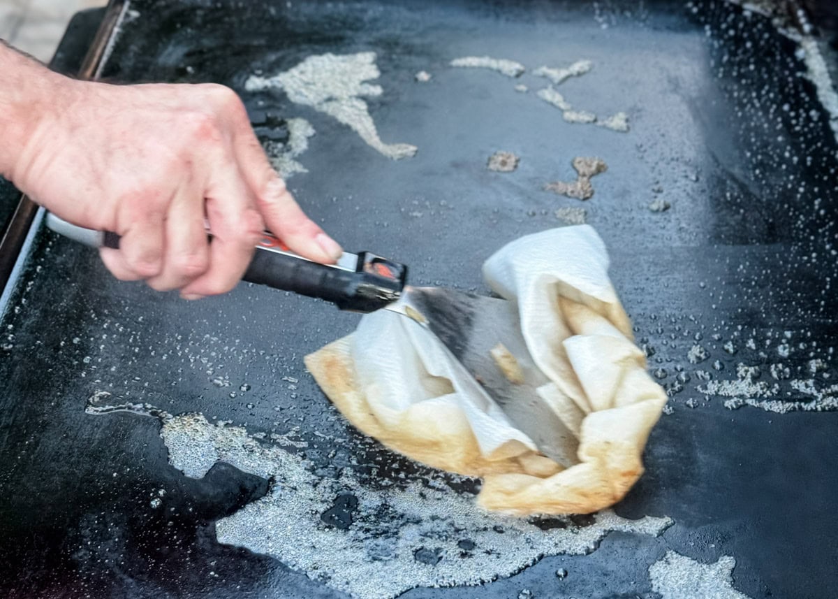 cleaning a Blackstone griddle with water, a spatula, and paper towels