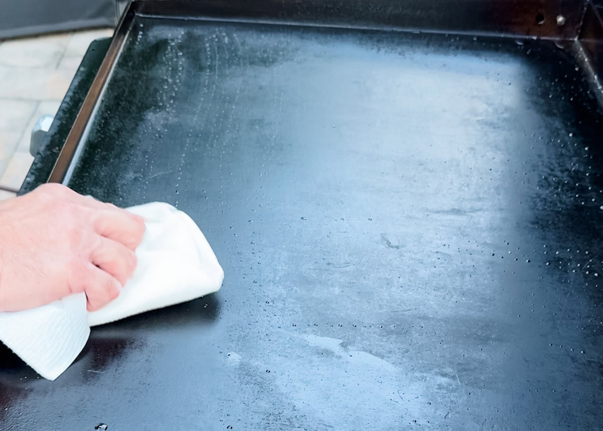 wiping a steamed griddle cooking surface with a paper towel to dry