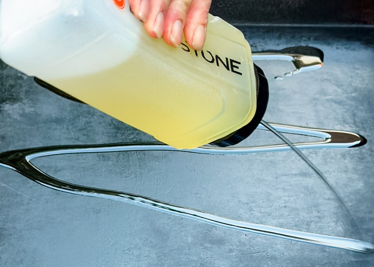 squirting vegetable oil onto a cleaned Blackstone griddle from a bottle