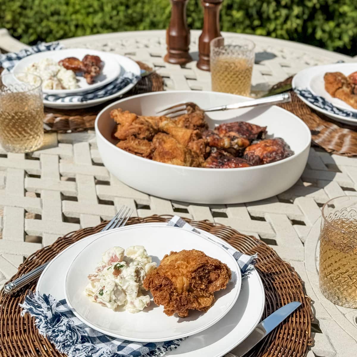 outdoor picnic table with table settings and a platter of fried and grilled chicken