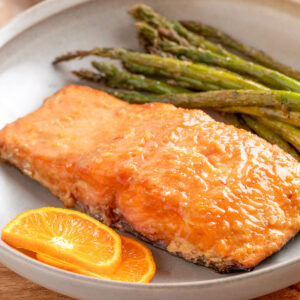 smoked salmon fillet with orange maple bourbon glaze on a plate with grilled asparagus and orange slices
