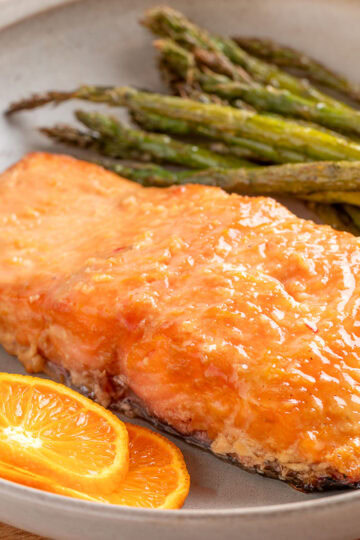 smoked salmon fillet with orange maple bourbon glaze on a plate with grilled asparagus and orange slices