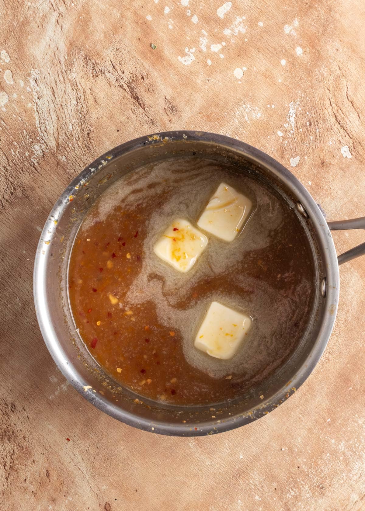 butter cubes added to orange maple bourbon glaze in a stainless steel pot