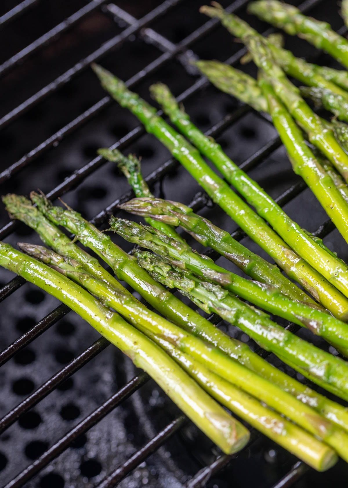 raw asparagus spears seasoned with olive oil, garlic salt, and pepper on a pellet grill