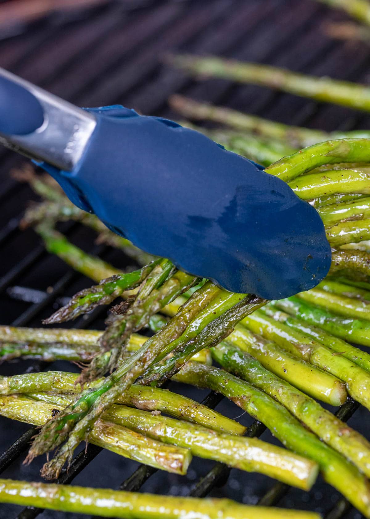 smoked asparagus being picked up from a pellet grill with blue silicone tongs
