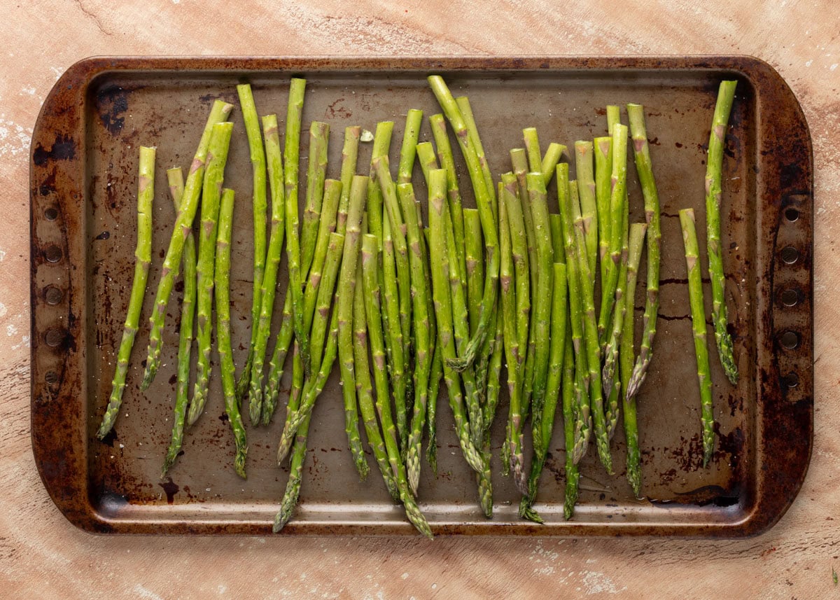 raw asparagus spears on a baking sheet with olive oil, garlic salt, and pepper