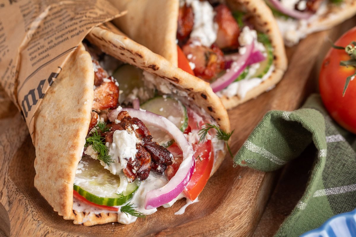 smoked chicken souvlaki pitas on a wood board wrapped with beige newsprint