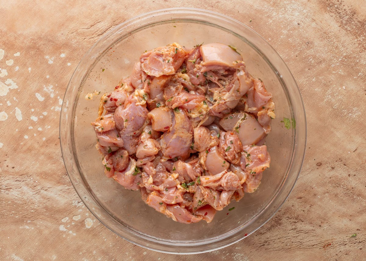 cubed chicken thighs tossed in marinade in a glass bowl