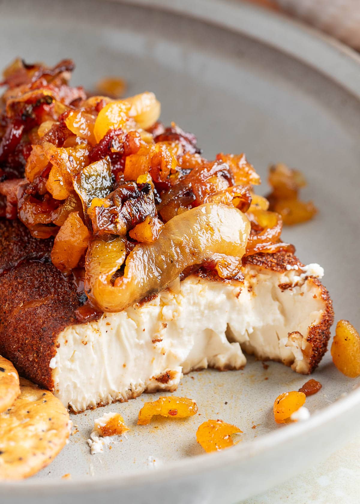 smoked cream cheese with bacon apricot and onion toppings on a plate. The cream cheese has been cut open to show the creamy center.