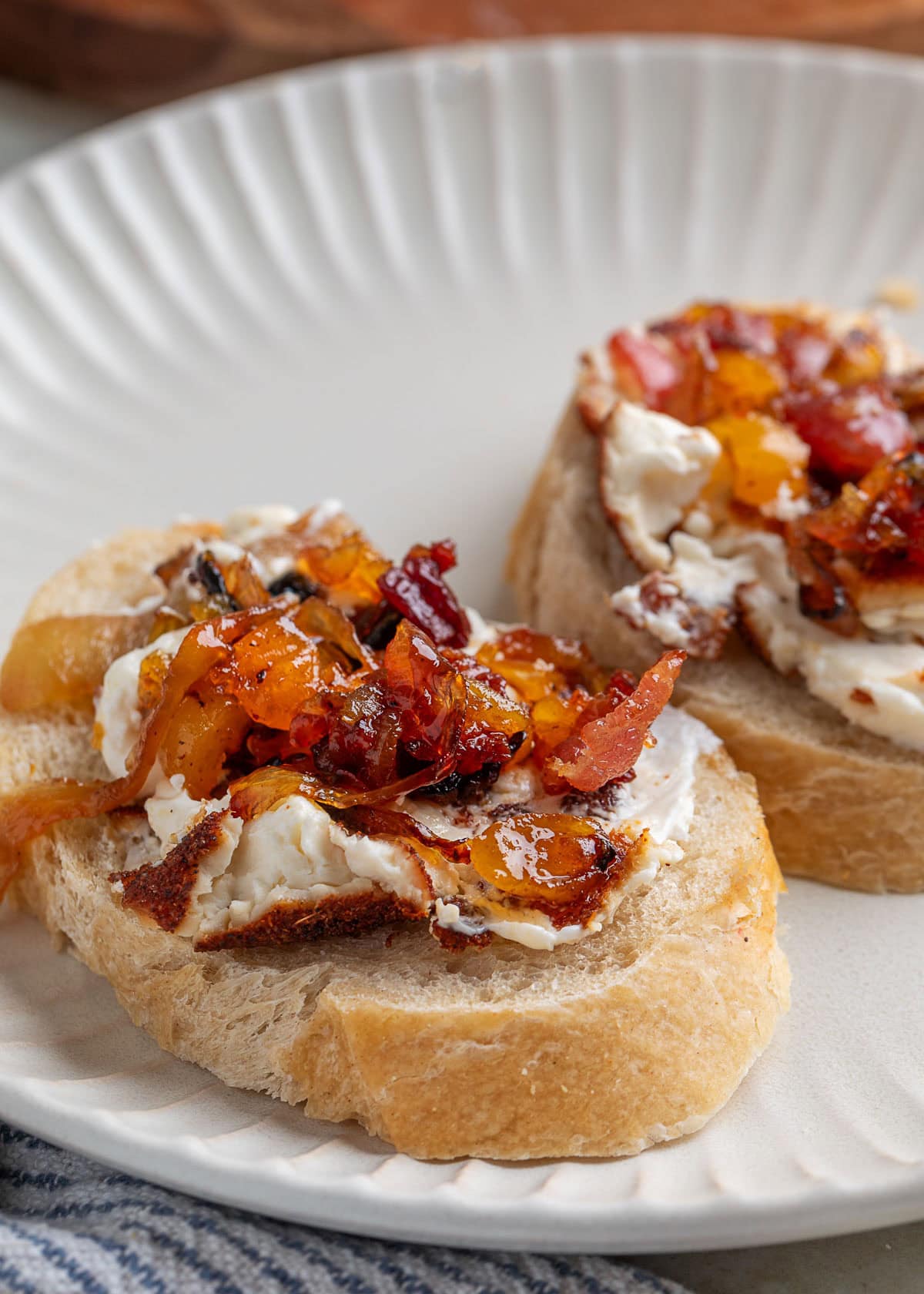 smoked cream cheese with bacon apricot onion topping on slices of crusty bread on a white plate