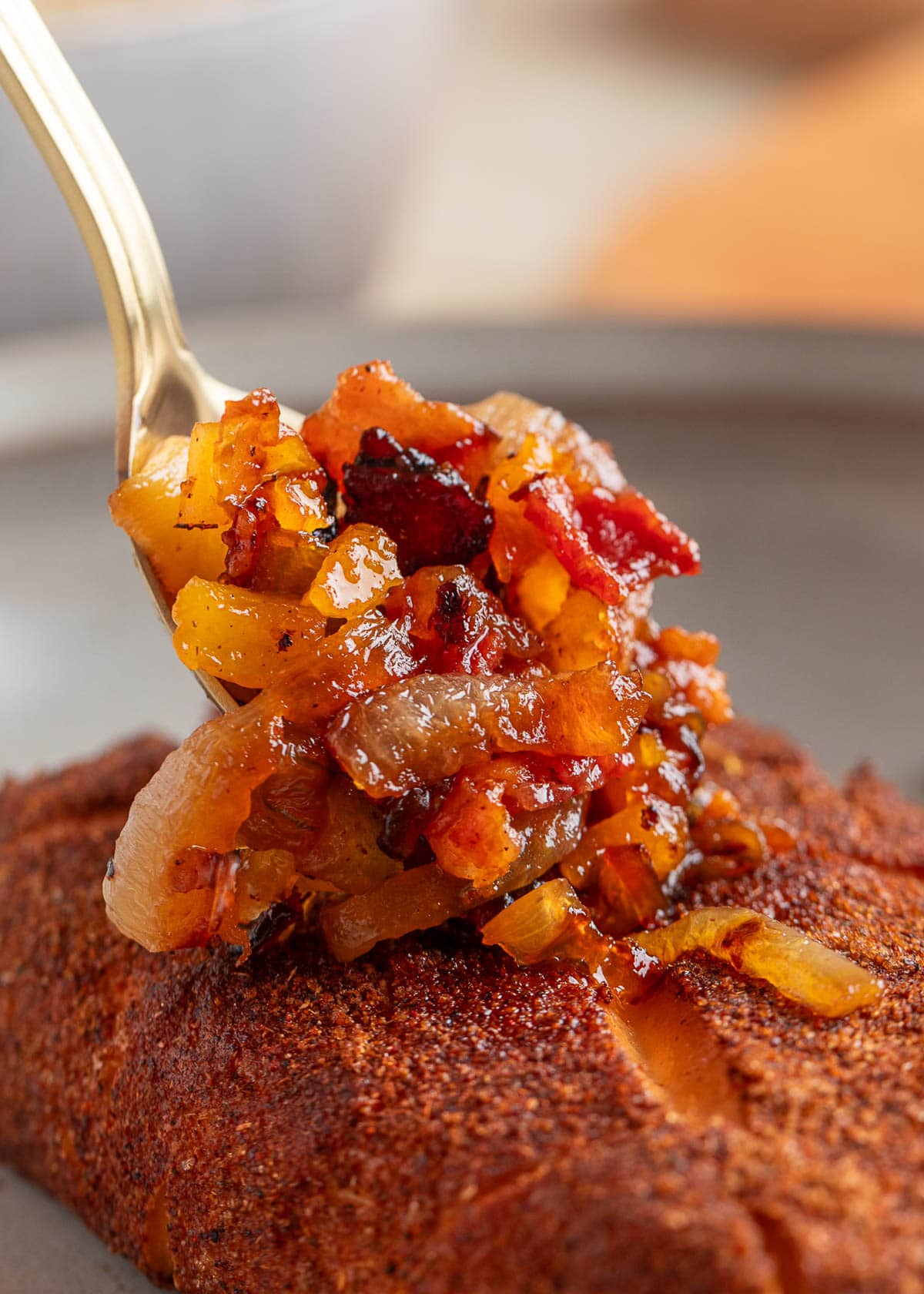 spooning bacon onion apricot topping over smoked cream cheese on a plate