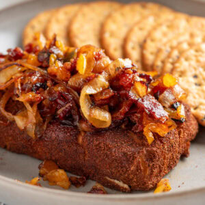 smoked cream cheese with bacon apricot and onion toppings on a plate with crackers