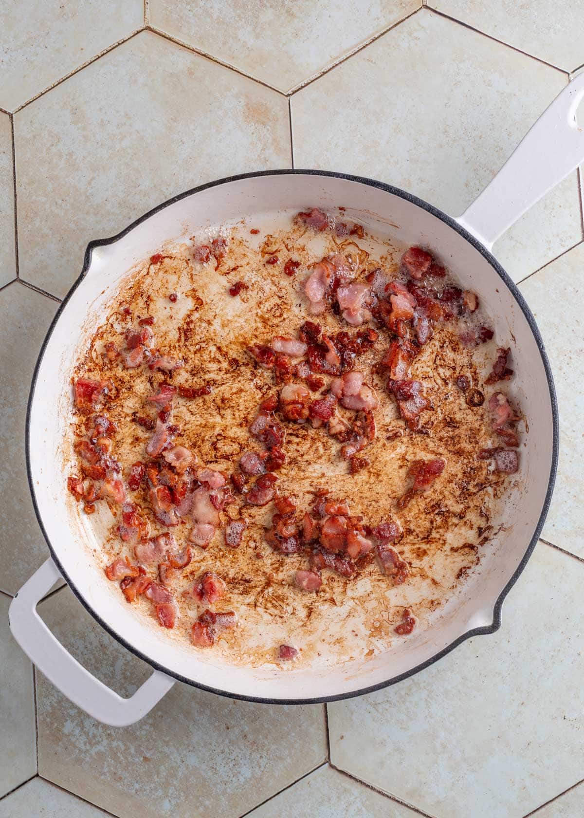 cooked chopped bacon in a white saute pan on an ivory tile surface
