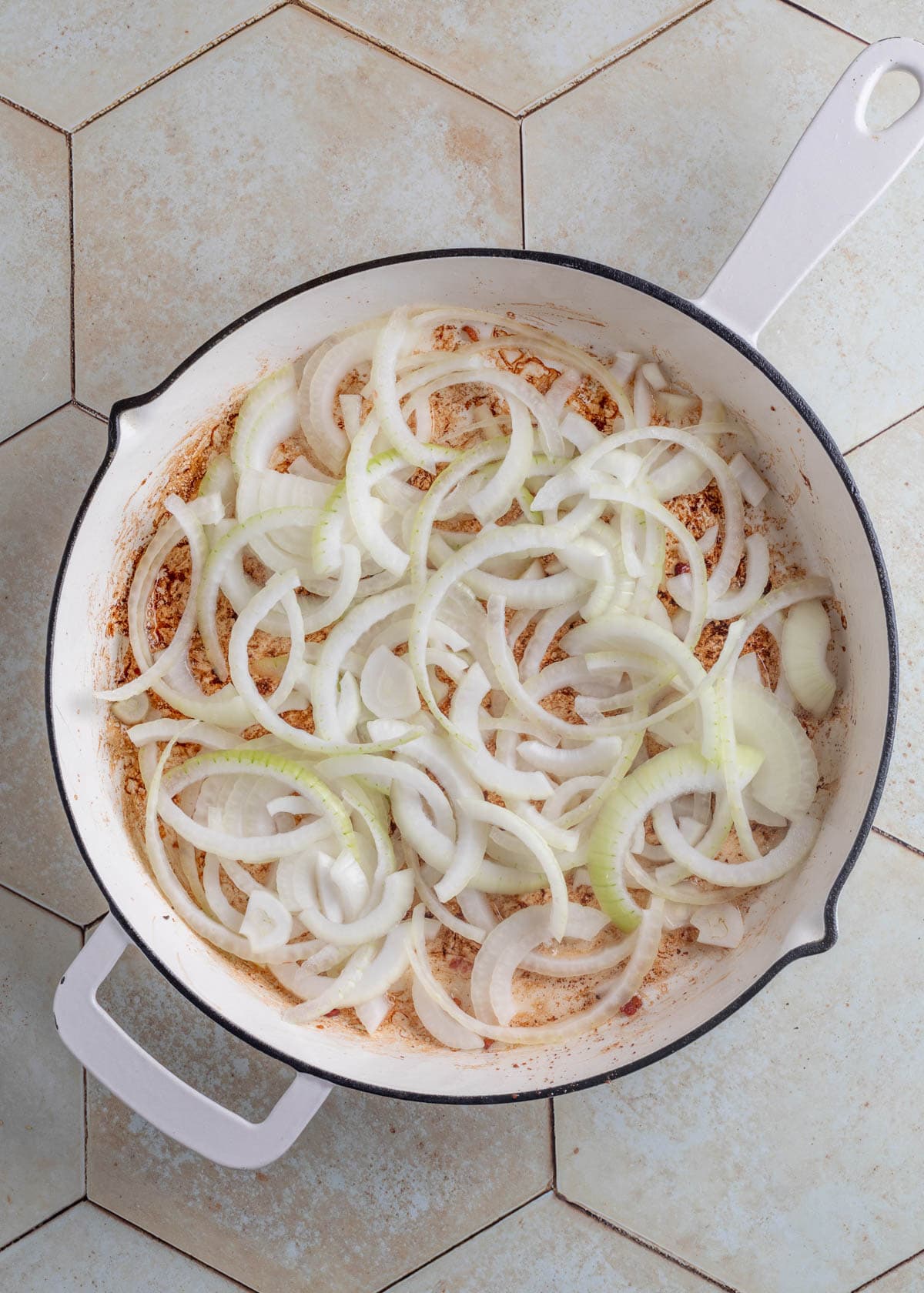 sliced onions in bacon drippings in a white saute pan on an ivory tile surface