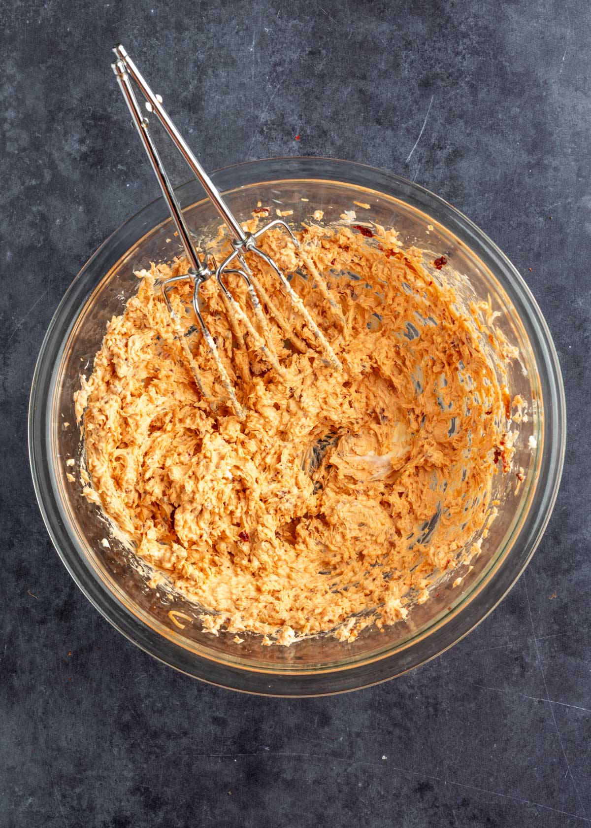 jalapeno popper chipotle gouda filling mixed in a glass bowl with two stainless steel mixer beaters on a dark gray surface