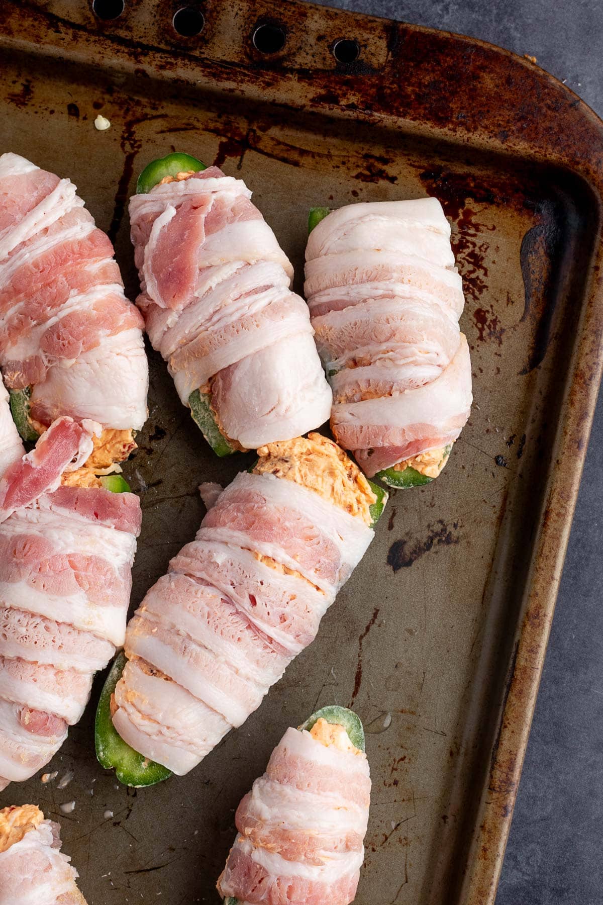 uncooked bacon wrapped jalapeno poppers on a baking sheet