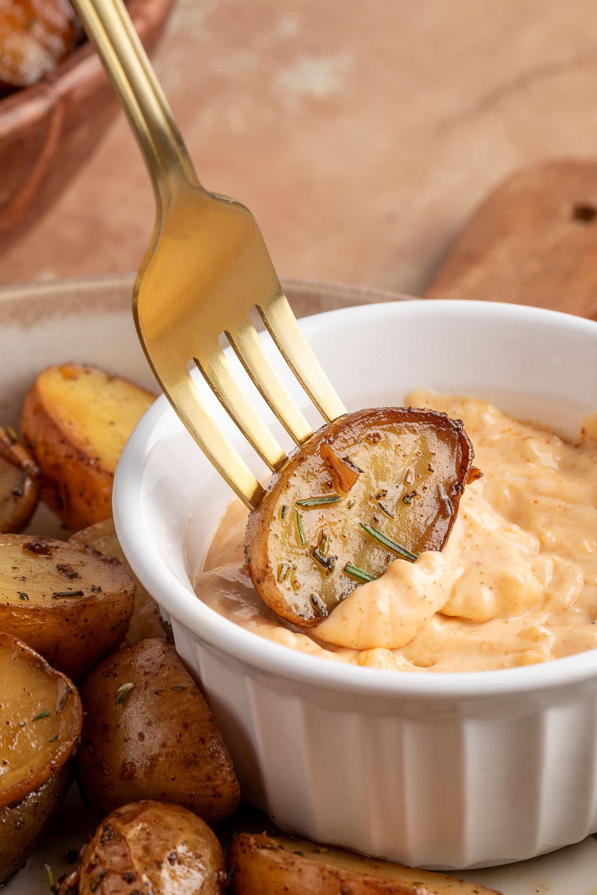 smoked potato half on a gold spoon being dipped into a white ramekin of garlic mayo dipping sauce