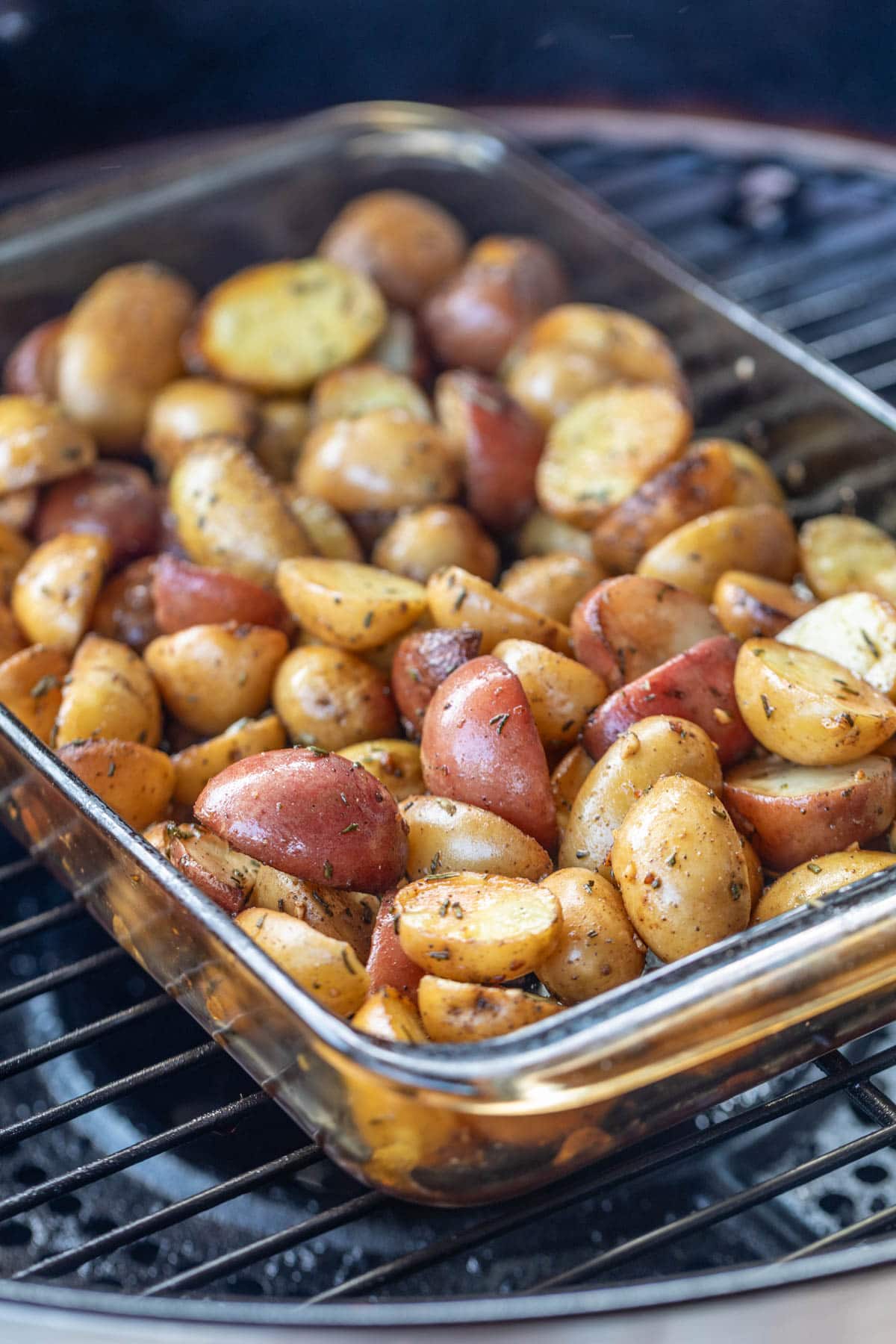 seasoned baby potatoes in a glass baking dish on a pellet grill