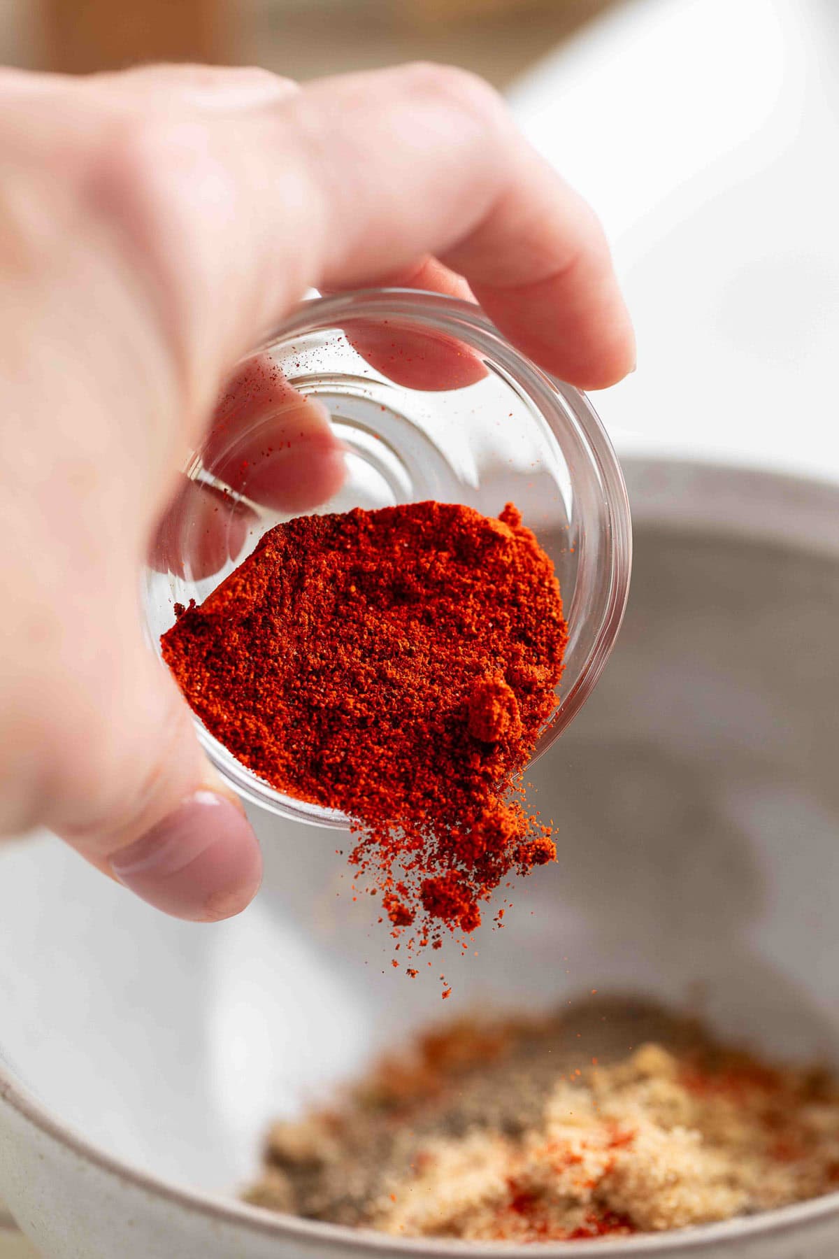 pouring smoked paprika from a small glass bowl into a white bowl of homemade fajita seasoning