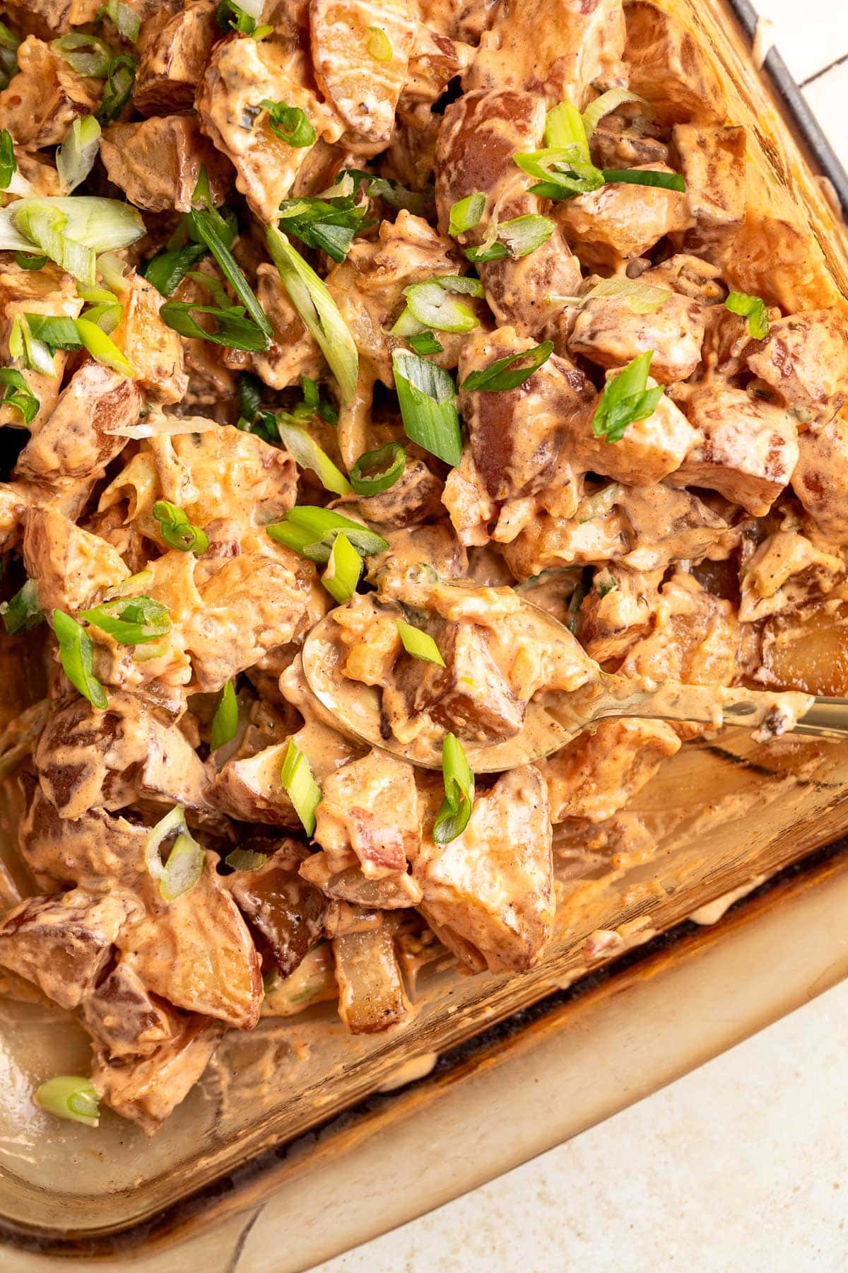 smoked potatoes mixed with bbq-mayo dressing and scallions in a glass pan with a gold spoon