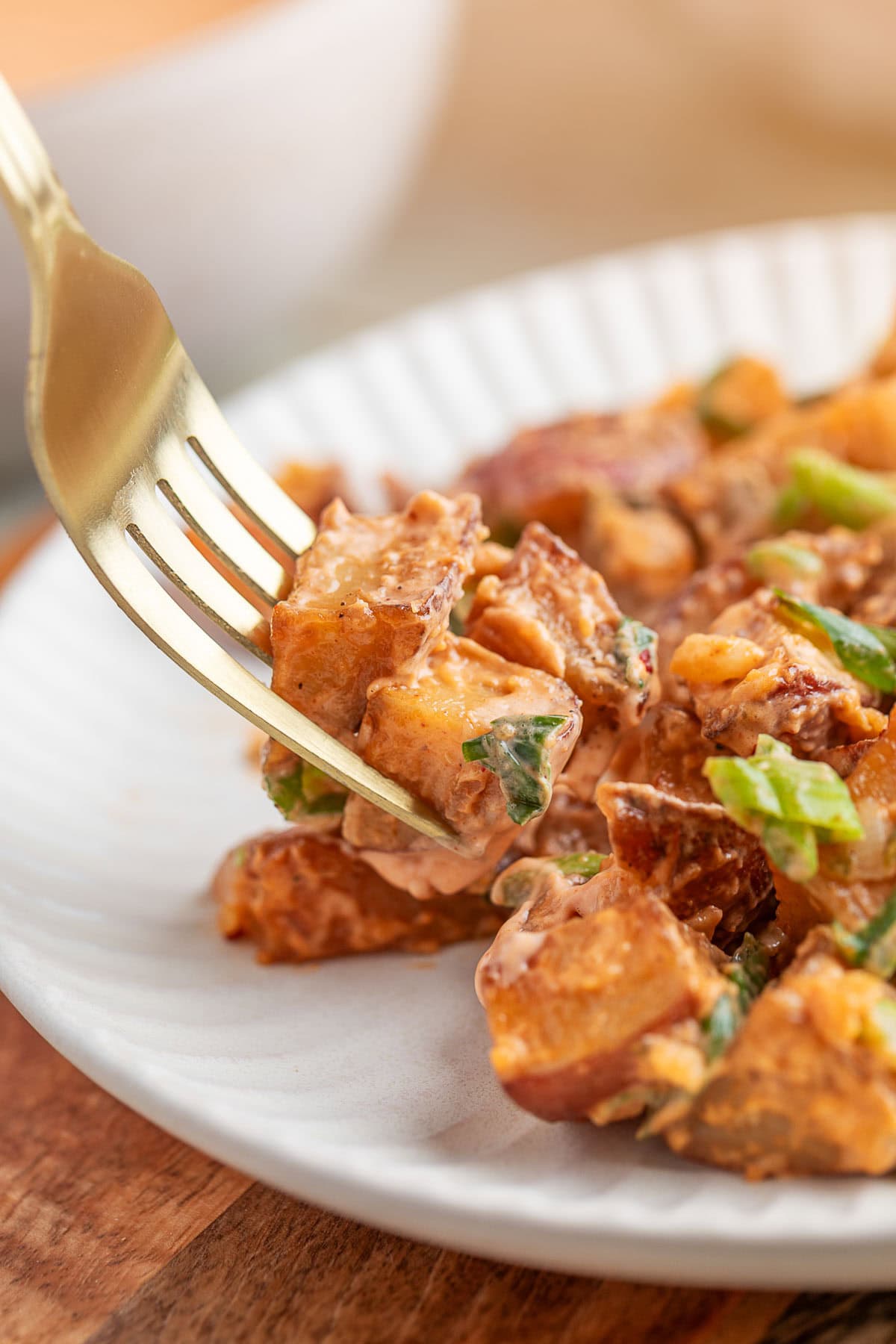 a gold forkful of smoked bbq potato salad being taken from a white plate