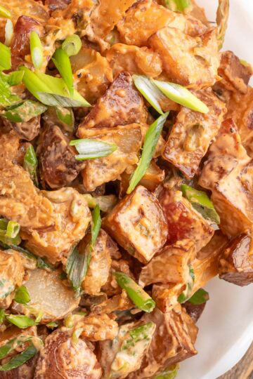 smoked bbq potato salad garnished with scallions in a white scalloped bowl on a wood serving board