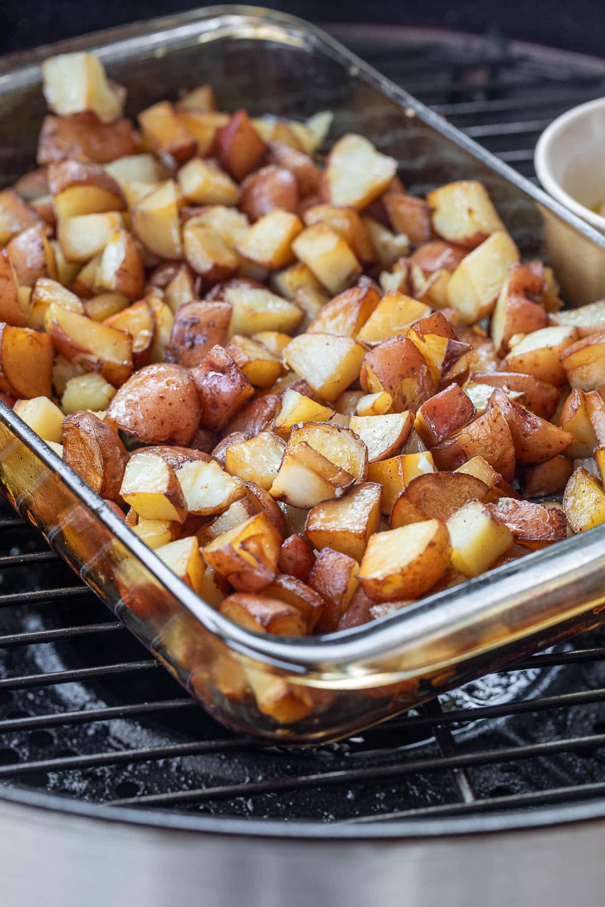 smoked cubed red potatoes in a glass baking dish on a pellet grill