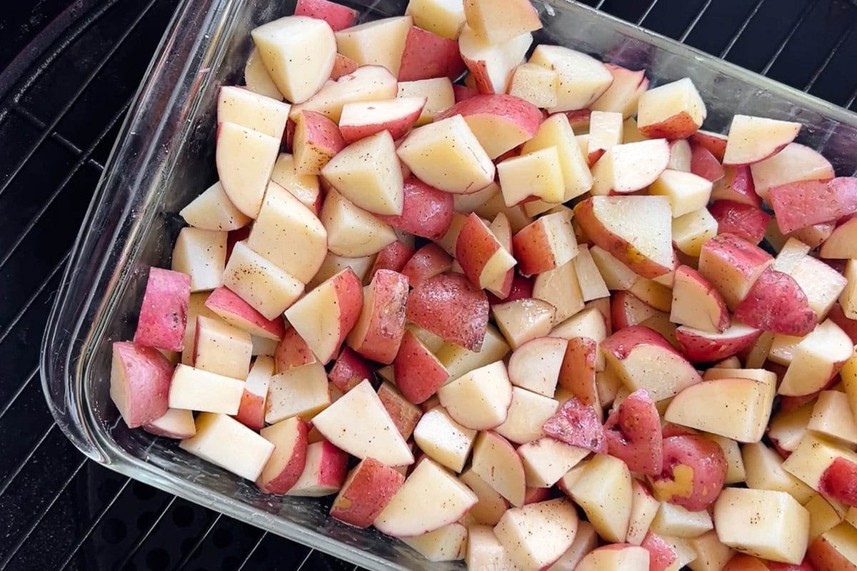 parcooked cubed red potatoes in a baking dish on a pellet grill