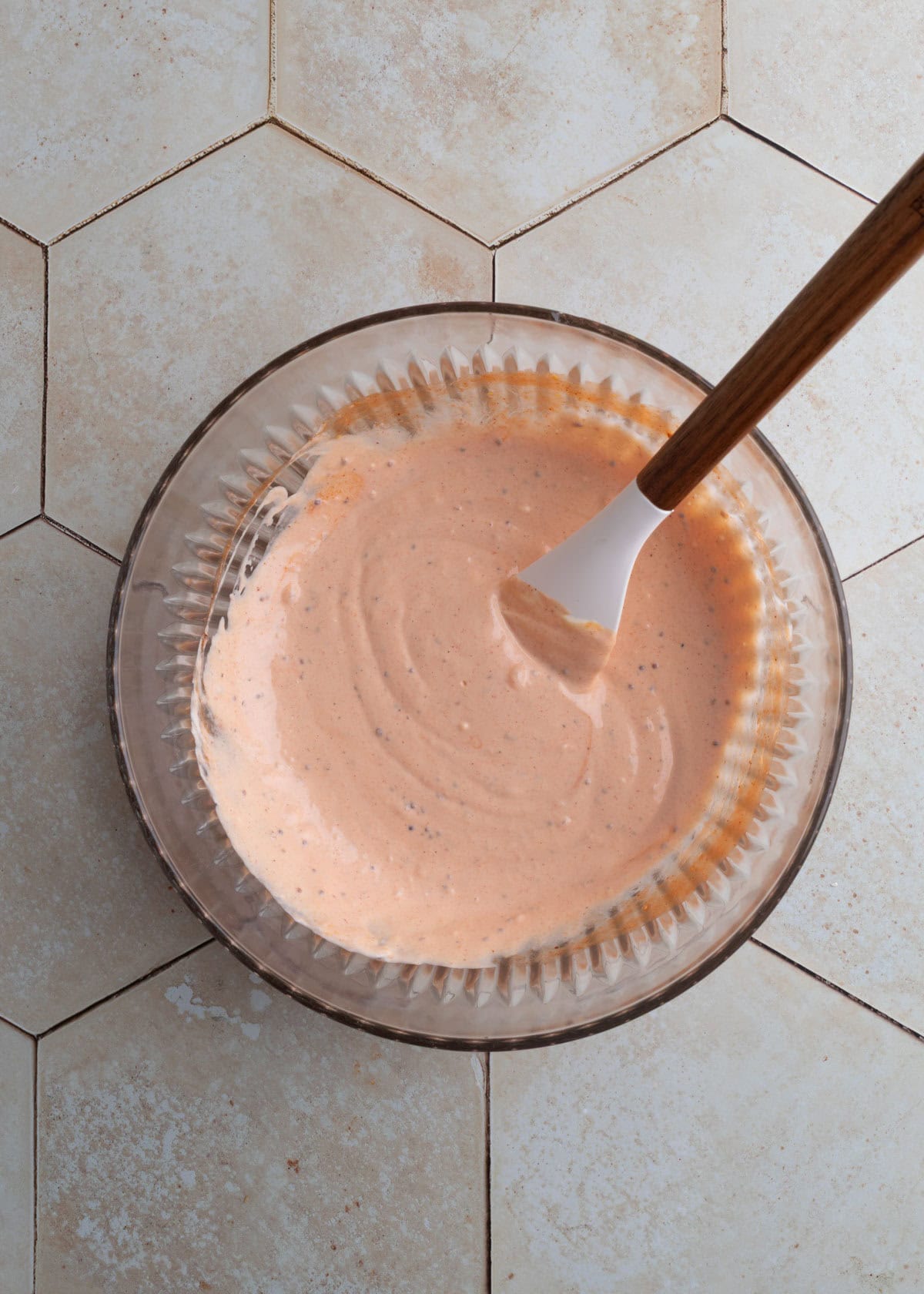 mixed dressing for smoked bbq potato salad in a glass bowl with a white rubber spatula on an ivory tile surface