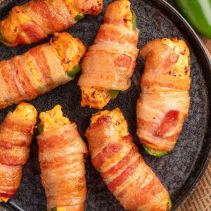 overhead of bacon wrapped smoked jalapeno poppers on a dark gray plate on top of a piece of beige newsprint