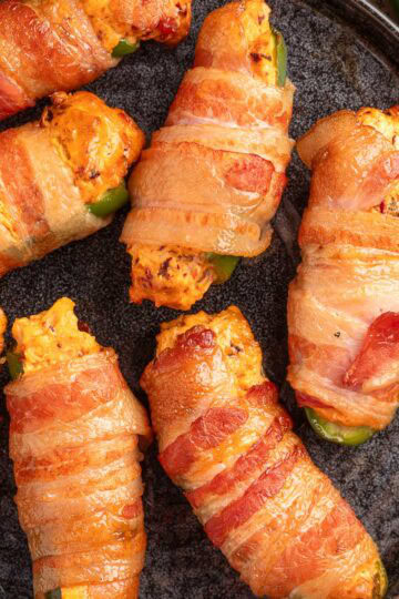 overhead of bacon wrapped smoked jalapeno poppers on a dark gray plate on top of a piece of beige newsprint